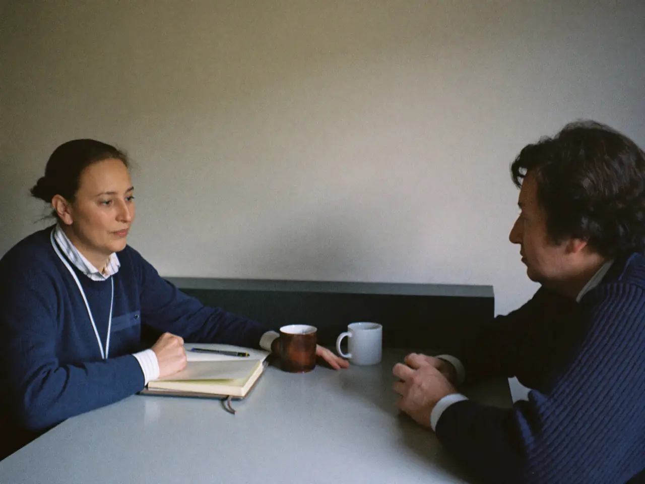 Two adults in a calm one to one conversation at a plain table.