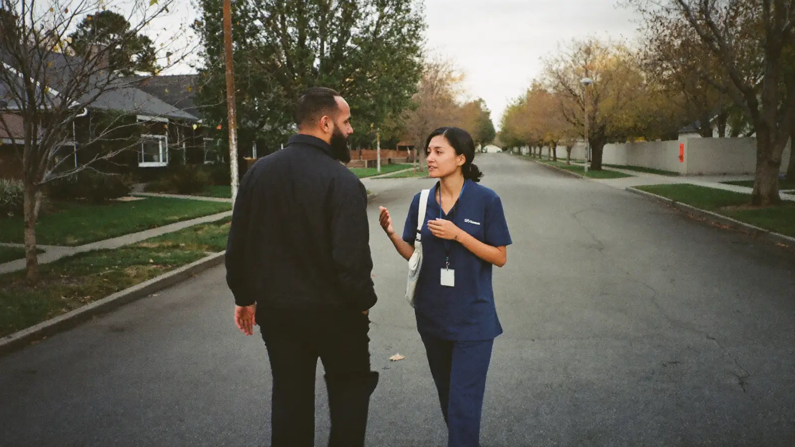 An adult and a support worker talking together on a quiet neighbourhood street.