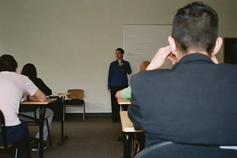 Adults seated at tables in a plain training room while someone explains at the front.