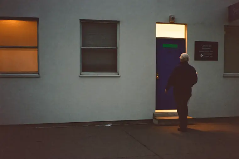 Warm light from the window of a small community office spilling onto the pavement at dusk.