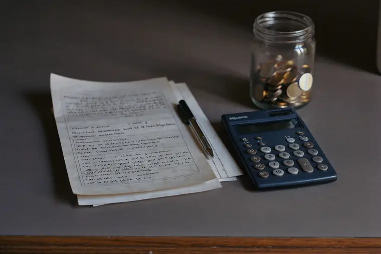 Household paperwork, a calculator and a coin jar on a kitchen table.