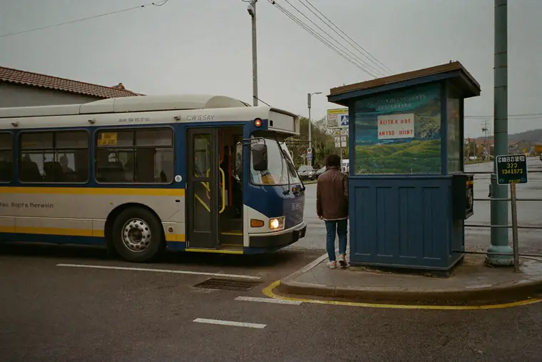 A city bus pulling up to an ordinary kerbside stop on a wet morning.