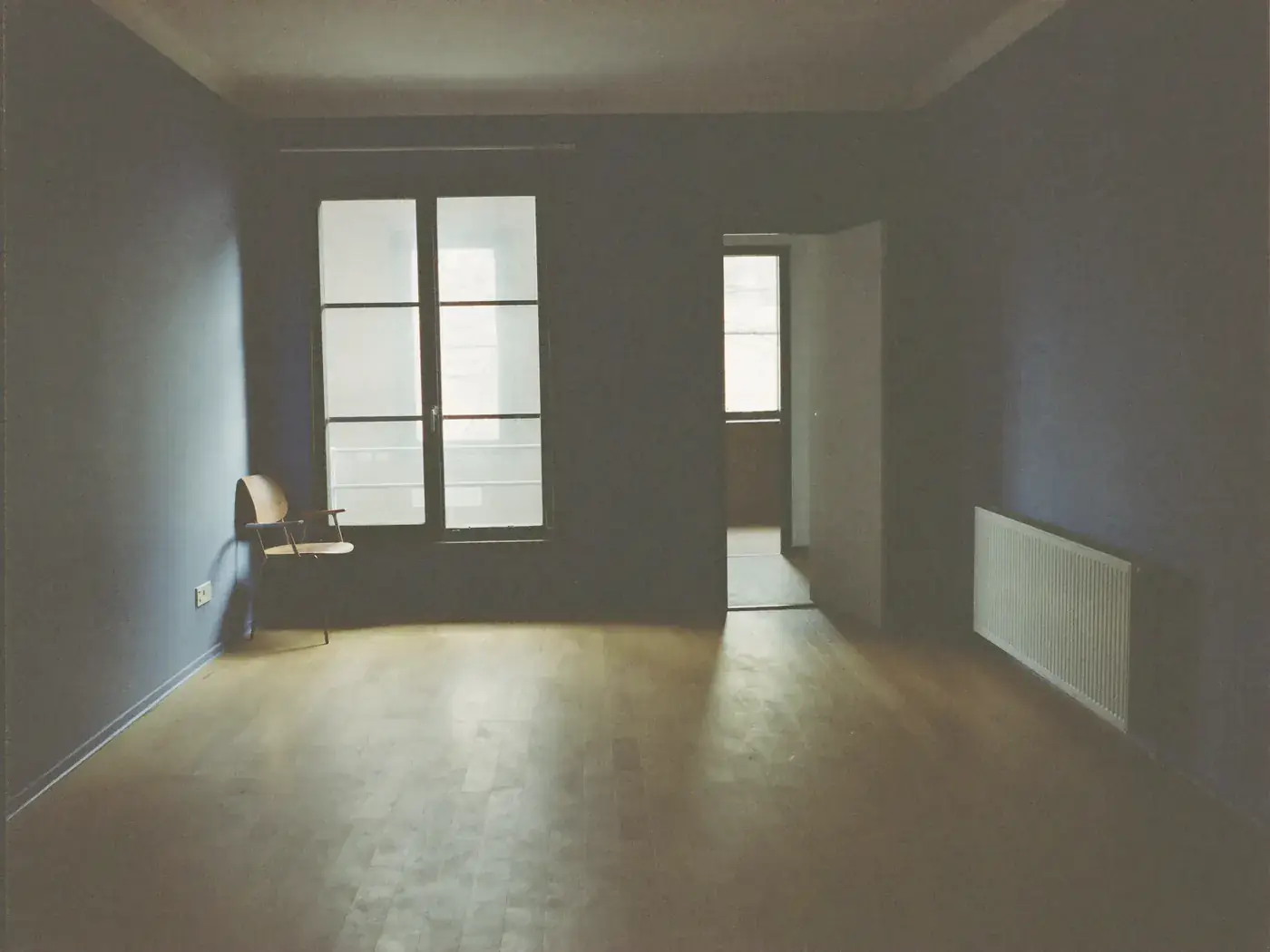 An empty, softly lit room in an ordinary house with daylight across a bare floor.
