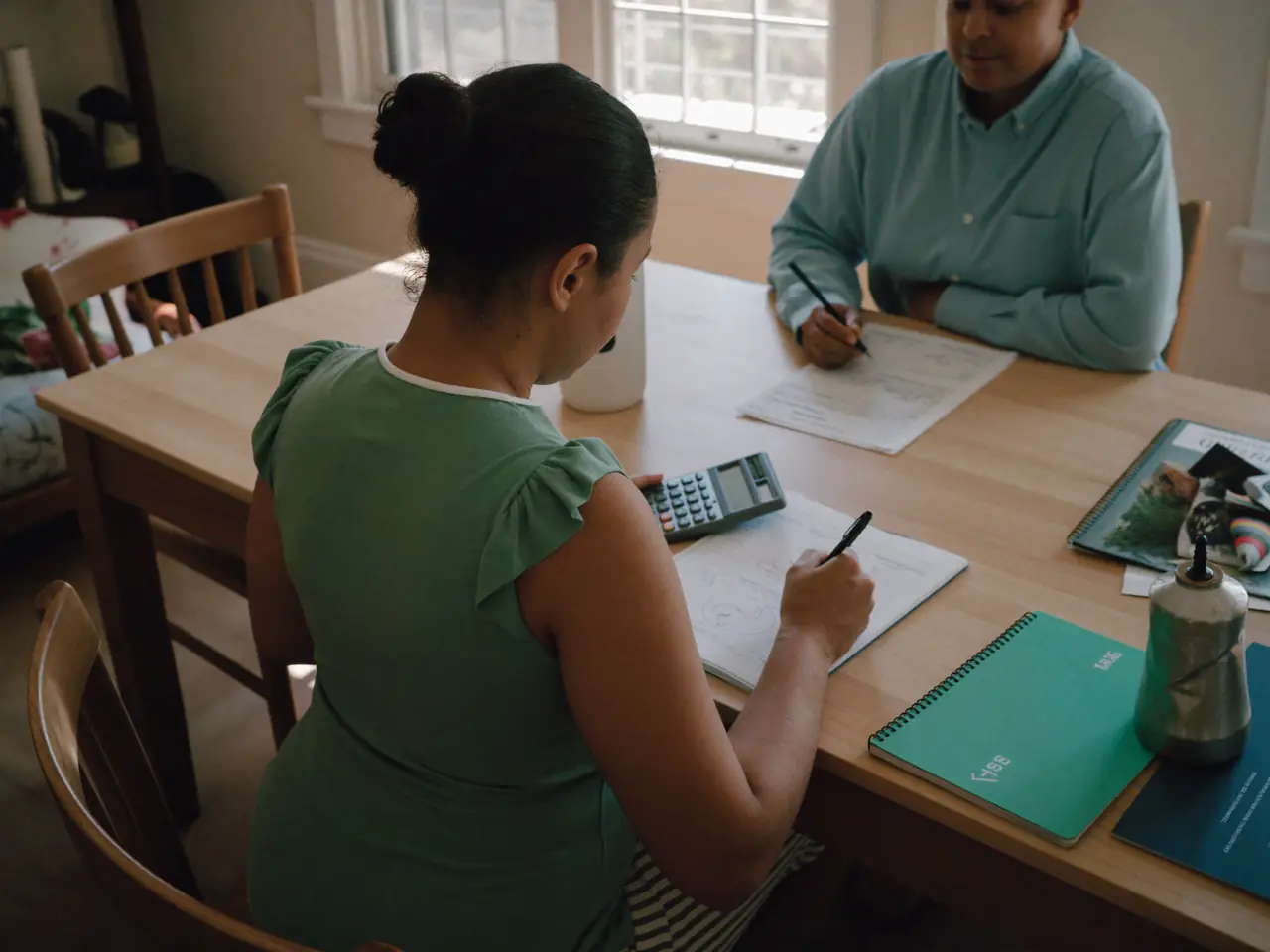 Two adults at a dining table working through a household budget with a notebook.